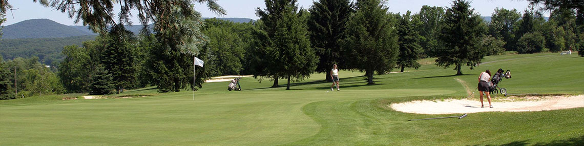 A woman strikes a ball out of a sand trap as another woman looks on